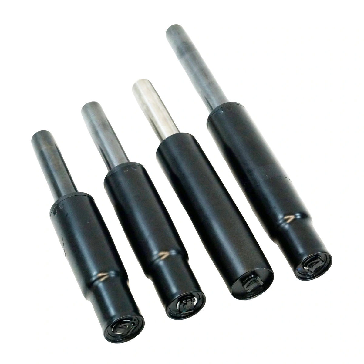 A set of four black chair cylinders lying parallel to each other on a white surface. Each cylinder features a slightly textured grip and a metallic shaft with a pointed tip, typically used for adjusting the height of an office chair