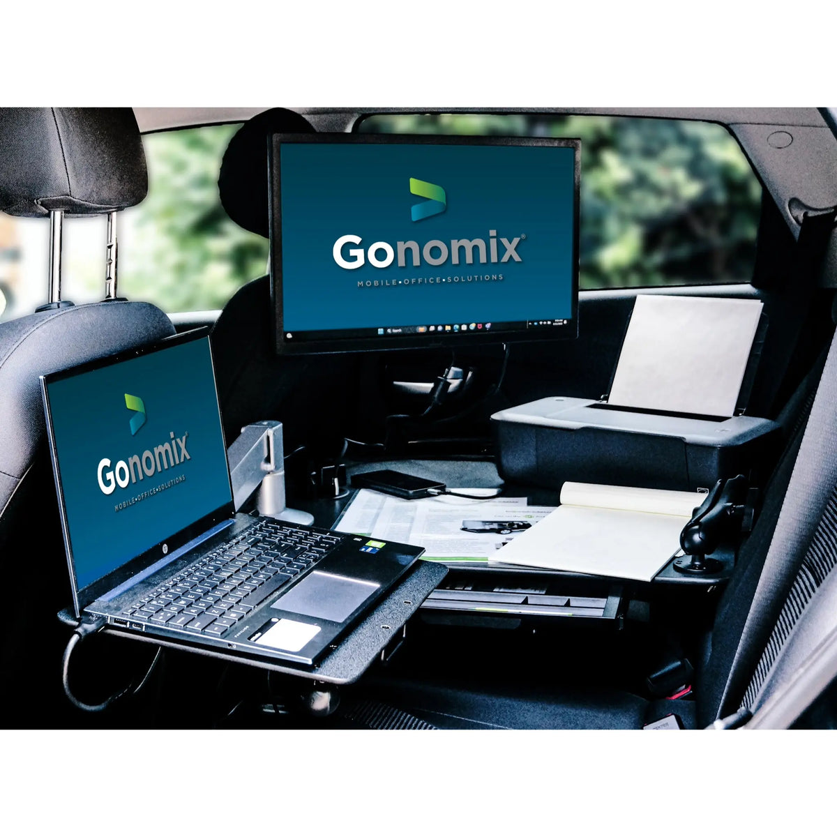 CarGo Vehicle Desk showing all of the features it can offer. A laptop is resting on top of the swing away extension arm away from the desk while the desk itself has documents and a printer on it while the drawer is also being shown.