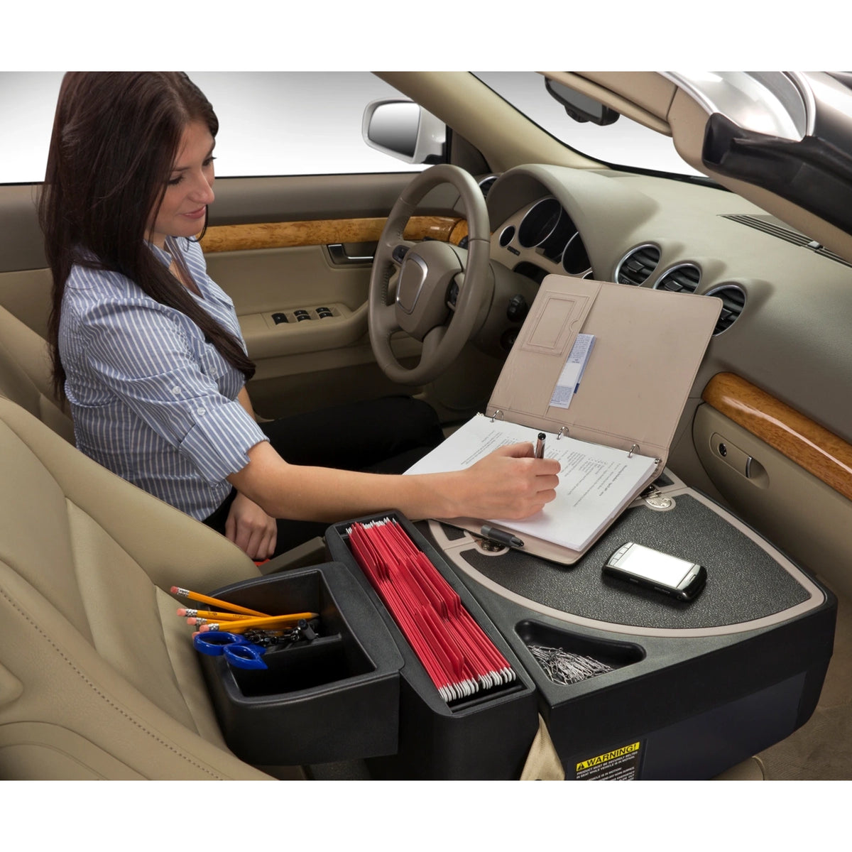 A women sitting in the drivers seat of a car using the express car desk to write in a notebook
