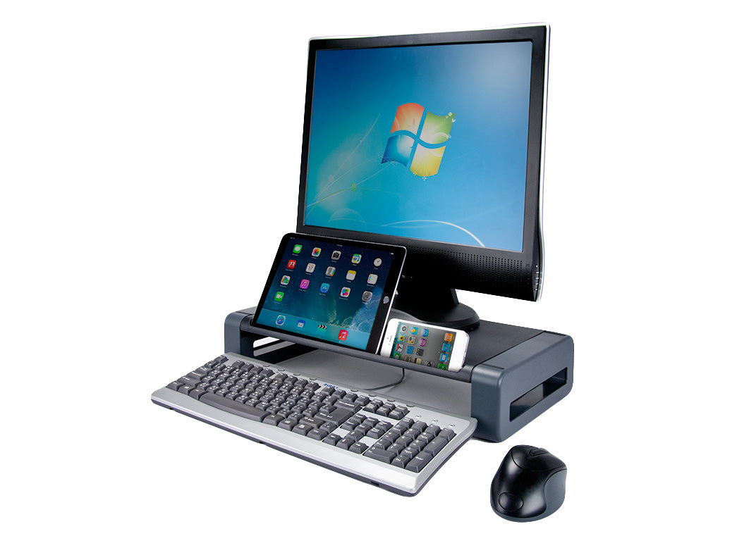 A rectangular monitor stand with a black surface tray and a gray stand. A black horizontal iPad and White iPhone rest in a small slot at the front. A large flatscreen monitor sits on the surface, a gray standard keyboard and black ergonomic mouse rest at the base