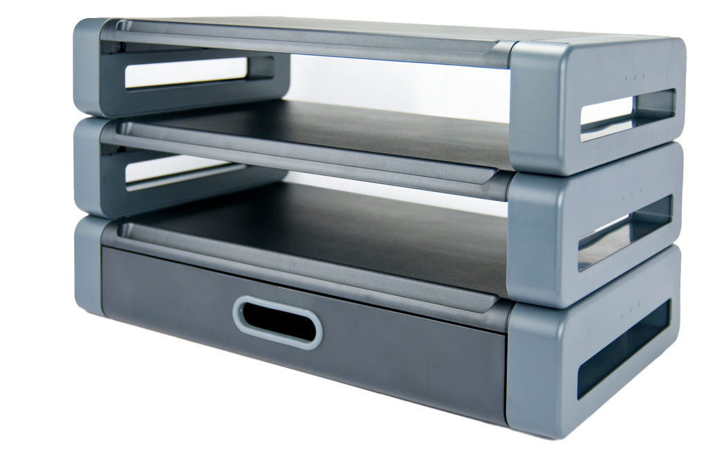 A stack of three gray and black plastic rectangular monitor stands. The bottom stand has a closed drawer with an oval shaped handle. Both the middle and top stands do not have a drawer