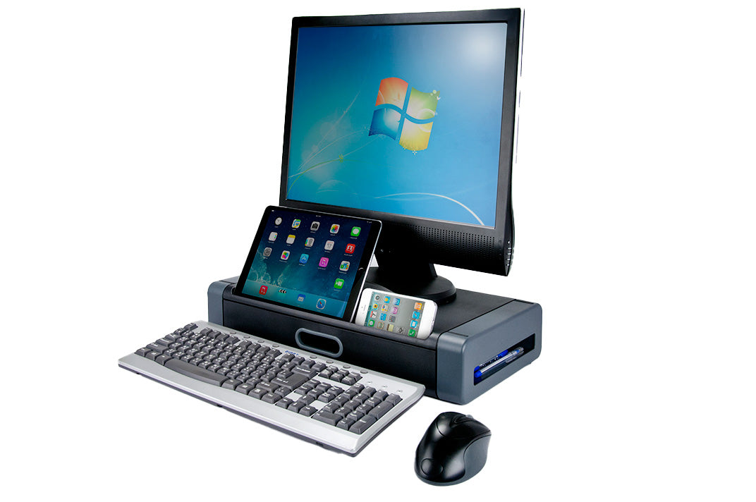 a gray and black plastic rectangular monitor stand and storage drawer with a flat top surface and two openings on the front side: an oval shaped handle and a long divot holding a black iPad and a white iPhone, both screens have colorful apps. A large black flat screen monitor rests on the top and a black standard keyboard and ergonomic mouse sit at the base of the stand