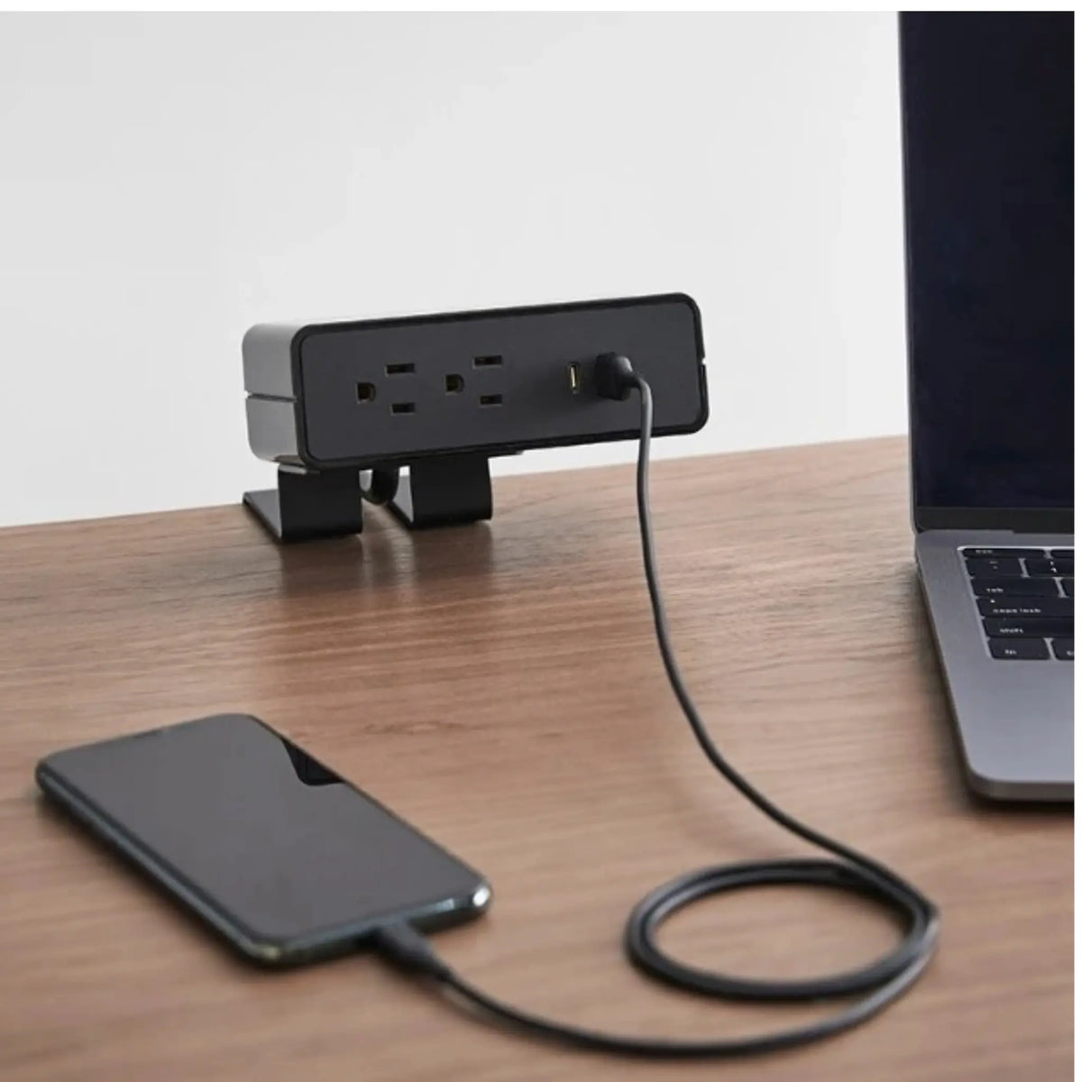 Black NeatHub Power Station in use on a wood desk plugged into a portable phone.