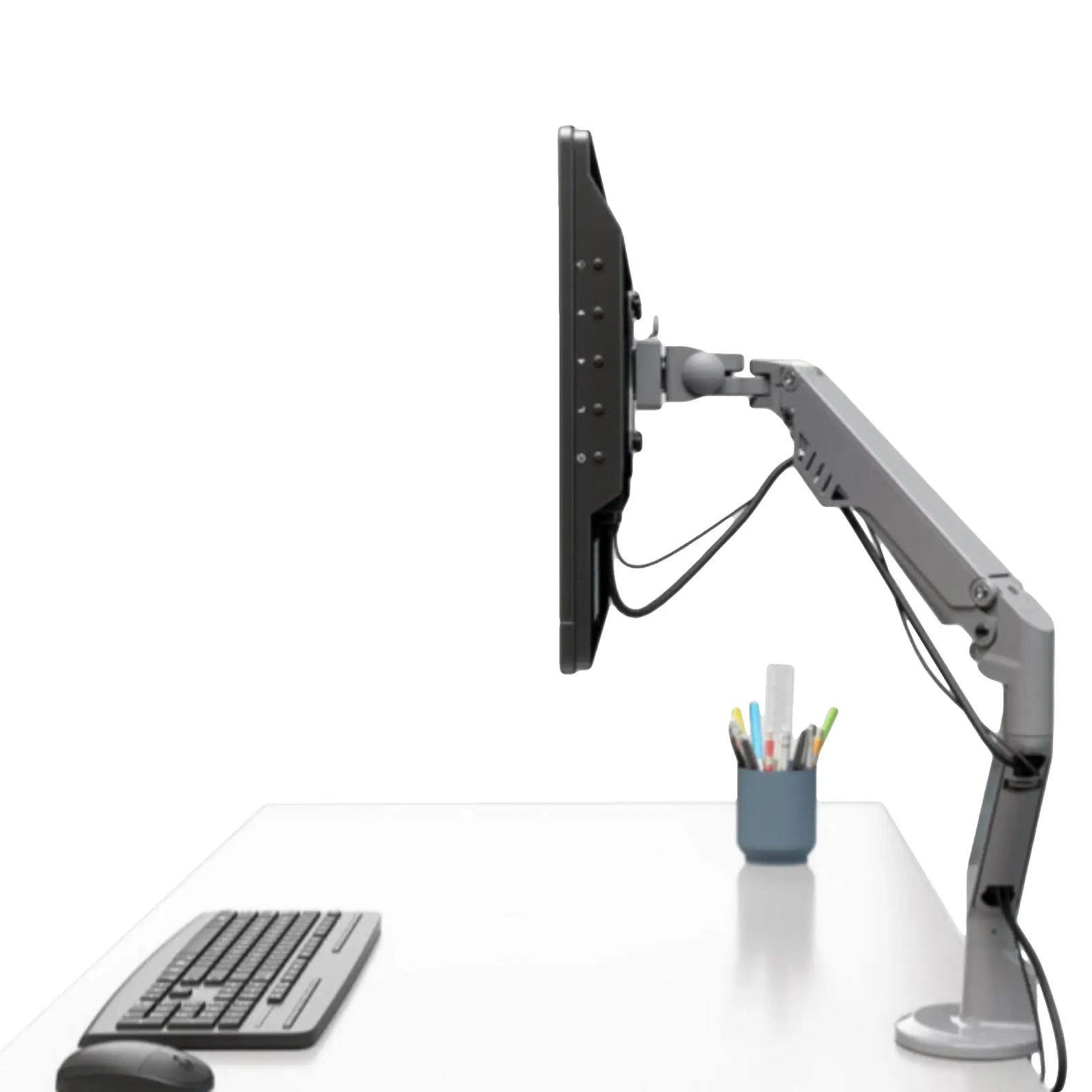 a silver articulated monitor mount holding a flat-screen monitor. The mount is attached to a white desk, which also has a keyboard, a mouse, and a holder with pens and pencils on it