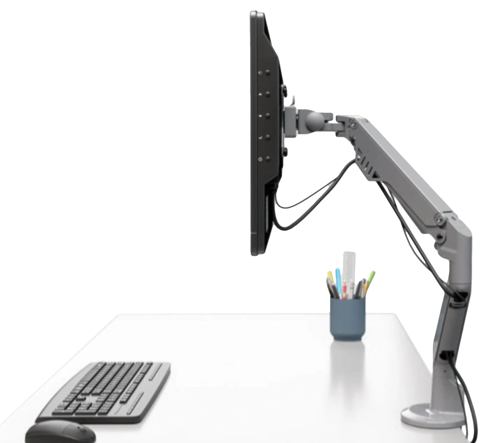 a silver articulated monitor mount holding a flat-screen monitor. The mount is attached to a white desk, which also has a keyboard, a mouse, and a holder with pens and pencils on it