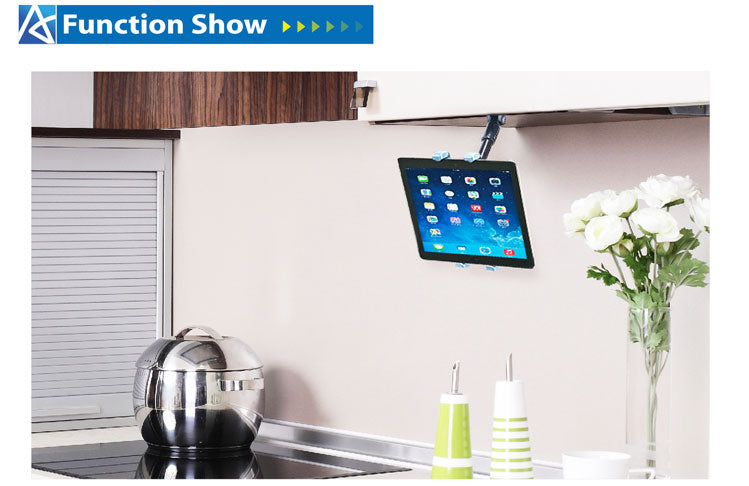 Under-cabinet mounted tablet holder in a modern kitchen, displaying a tablet with various apps, above a countertop with a kettle, containers, and a vase of white flowers.