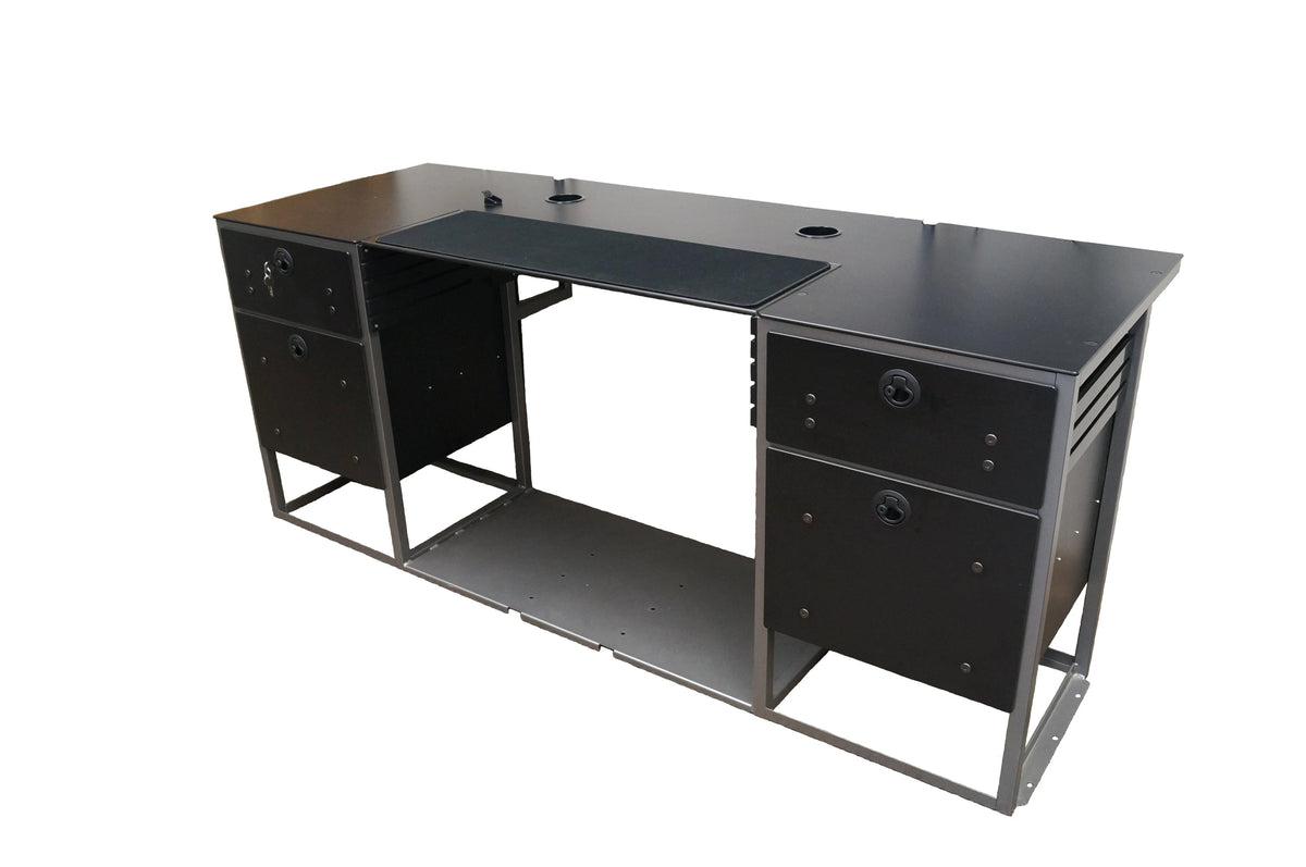 A large flat desk with a black work surface. It features black fabric in the middle meant as a grip for a keyboard and mouse. It has two empty grommet holes located on both the upper right and left-hand sides of the surface. The base of the desk is made of 2 sets of black drawers on each side of an open space meant for a chair. The bottom of the desk is connected together with a large sheet of gray metal.