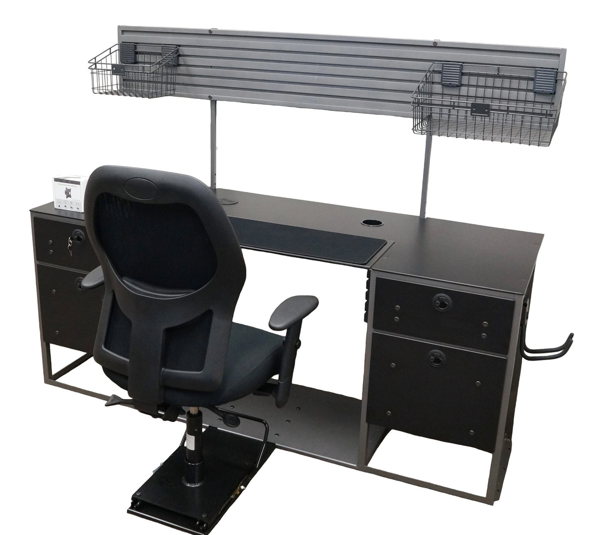 A large flat desk with a black work surface, a hutch, and a connected black chair mounted on a black sliding seat base. The surface features black fabric in the middle and two empty grommet holes. Mounted to the back of the desk is a large gray hutch with groves and a monitor mount. The base of the desk is made of 2 sets of black drawers on each side of an open space for the chair. The bottom of the desk is connected together with a large sheet of gray metal to which the sliding black chair is mounted. 