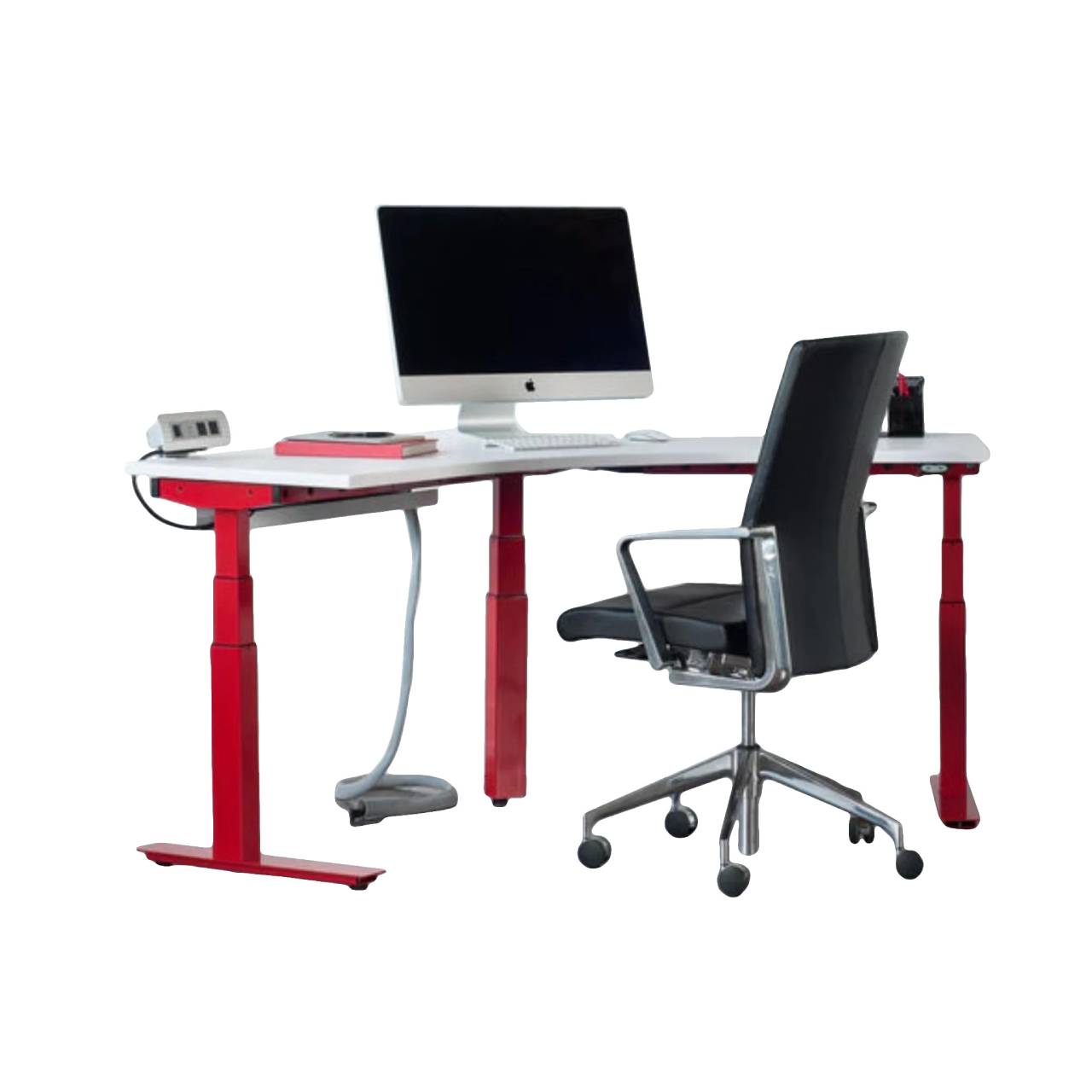 a modern workspace setup featuring a height-adjustable desk with red legs and a white tabletop. On the desk, there is an iMac computer on a stand, a white phone on a dock, and some papers to the left of the computer. There is also an office chair with black upholstery and armrests in front of the desk