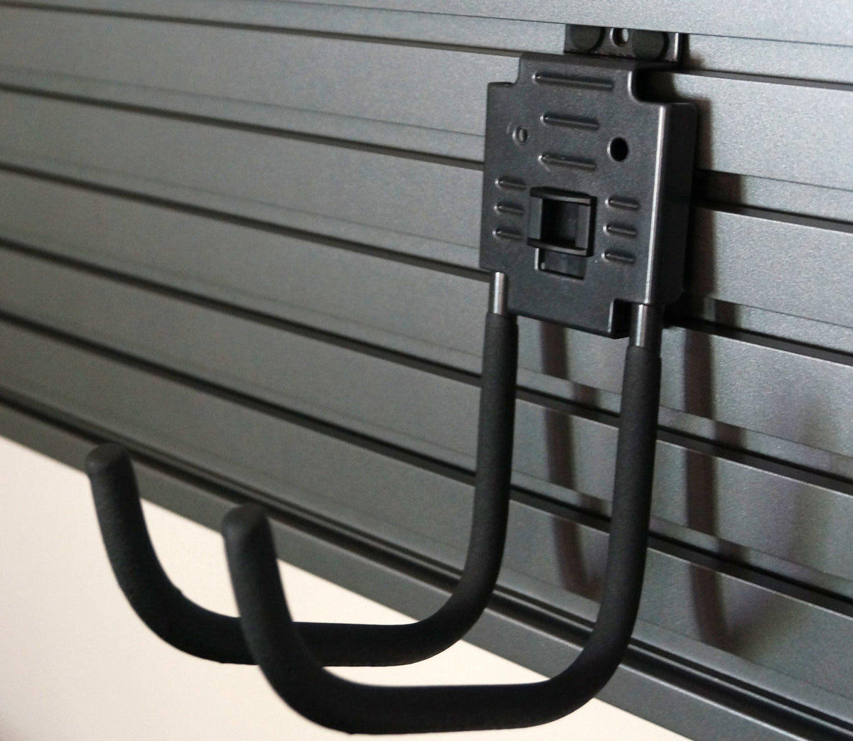 a black J shaped hook featuring a rectangular metal piece mounted to a large ridged gray metal slatwall hutch